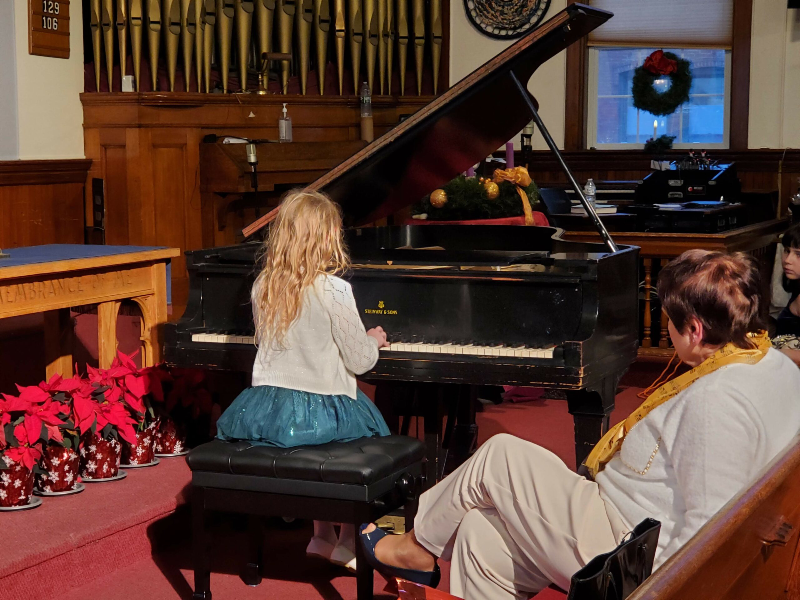 A student sits at the piano playing at the recital as Miss Irena watches